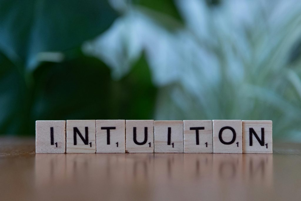 Wooden letter tiles spelling 'Intuition' on a blurred green background.